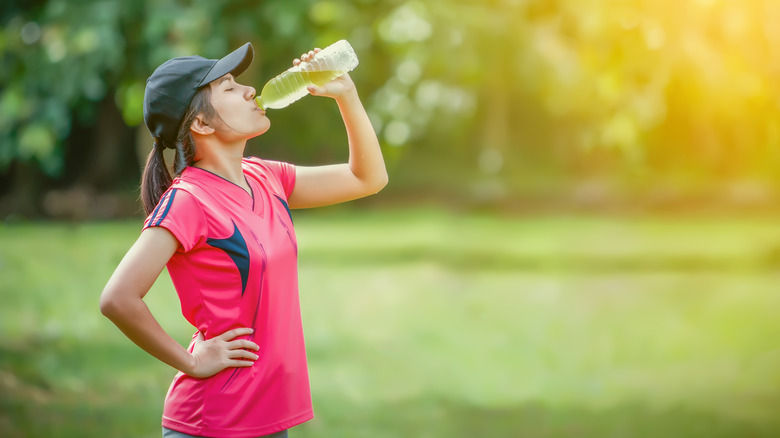 A woman drinks an electrolyte drink while exercising