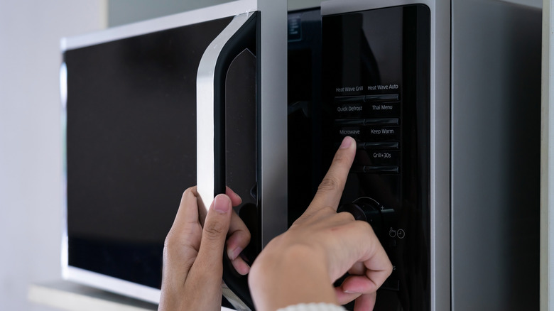 Hand touching the microwave button on a microwave