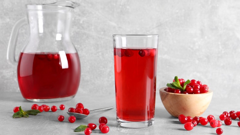 glass of cranberry juice surrounded by cranberries and a pitcher of juice