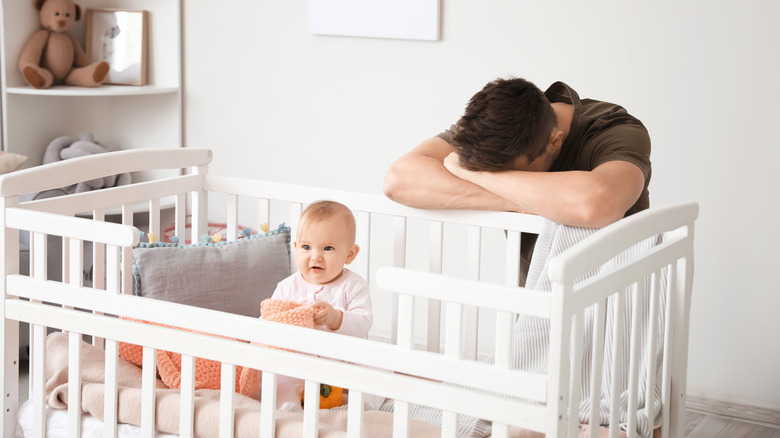 Tired young father next to baby in crib