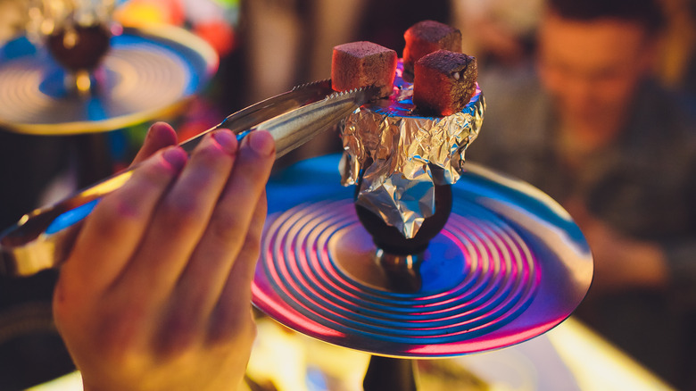 Hand using tongs to place flavored tobacco on heated hookah