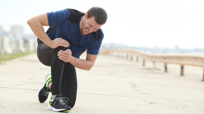 man holding injured knee while running outside