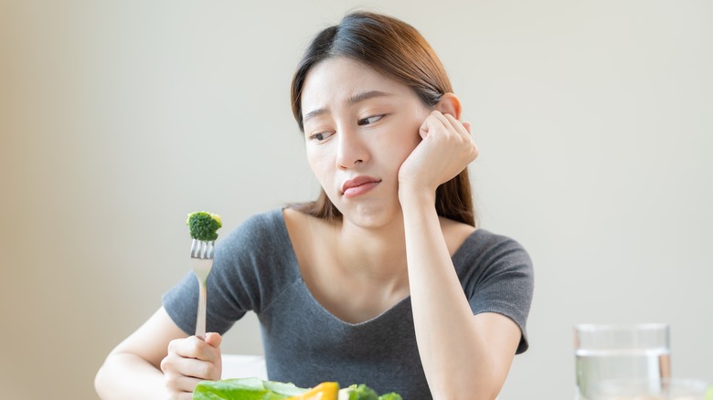 An unhappy woman looks at broccoli on her fork