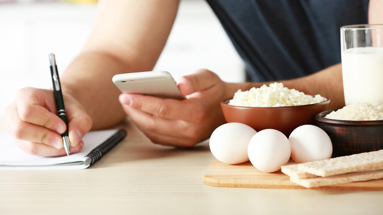 Person uses smart phone and notepad to track calories surrounded by healthy food