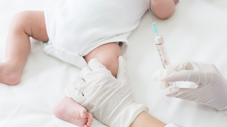 Doctor prepares vaccination and holds thigh of infant