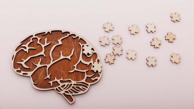 Puzzle pieces leading to a stylized brain profile made of wood 