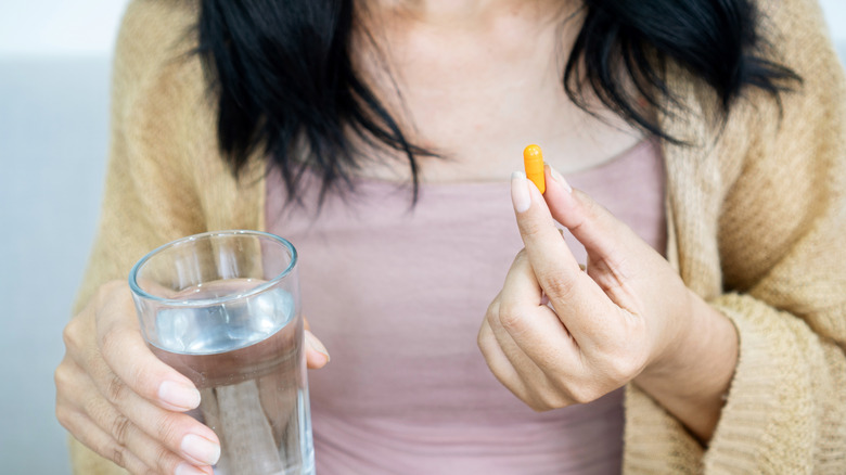 Woman holding curcumin supplement and water glass