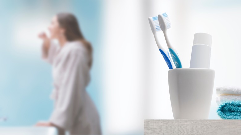 toothbrush and toothpaste with woman brushing teeth in background