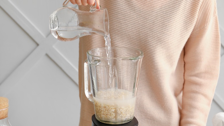 Hand pouring water and oats into blender