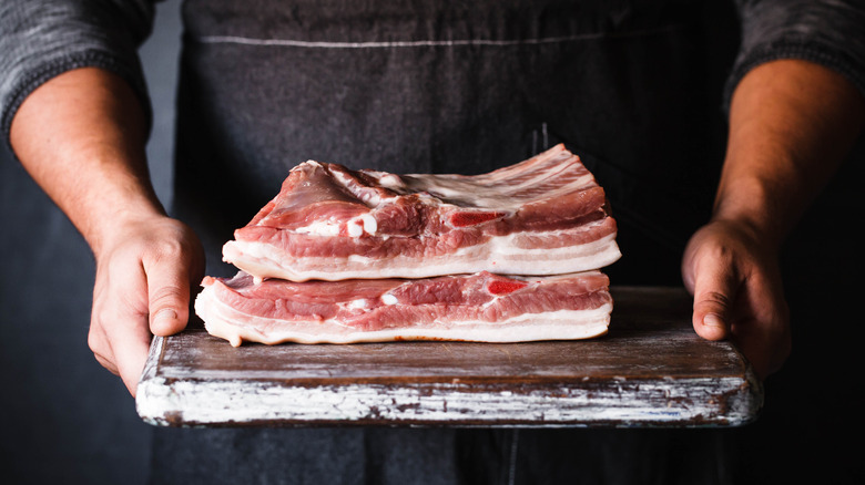 butcher holding platter of pork belly