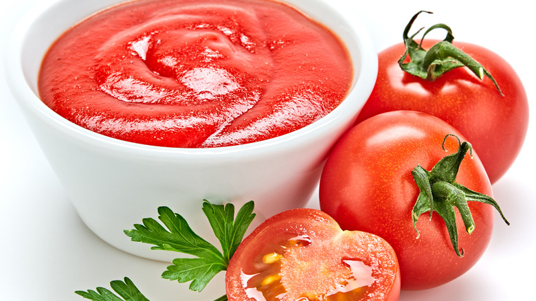 tomato puree in a bowl next to fresh cut tomatoes