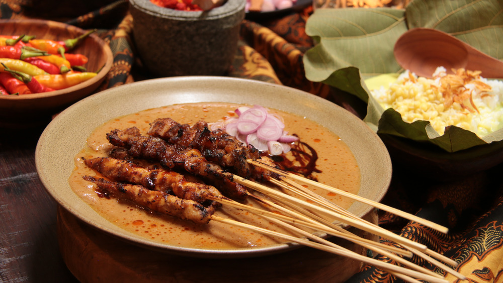 Several plates of food including chicken satay skewers