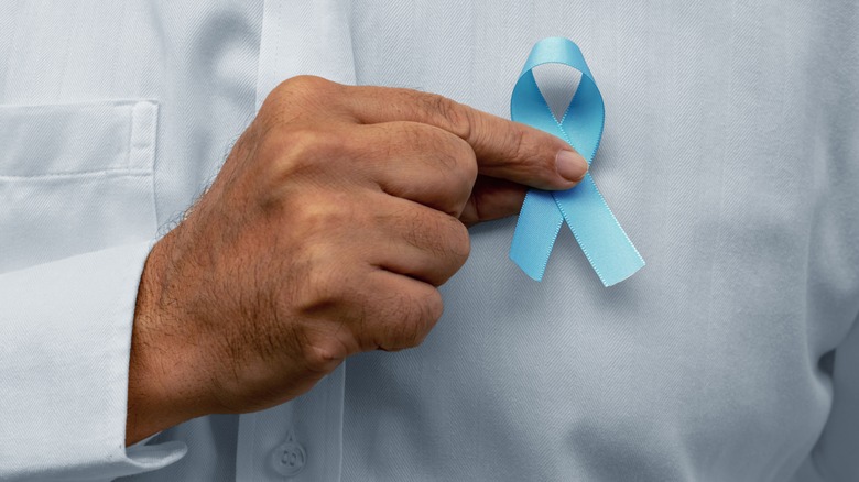Close-up of hand holding a blue ribbon in front of their shirt for prostate cancer awareness