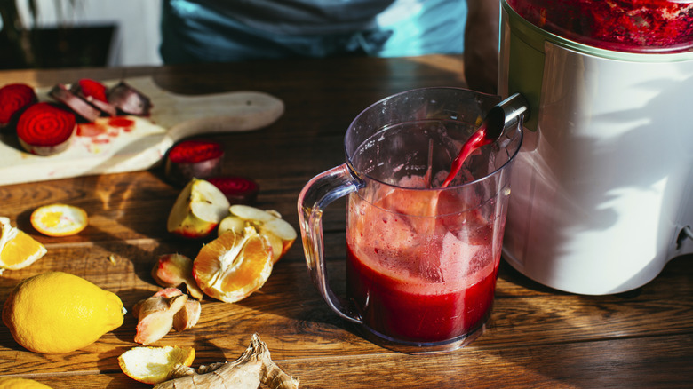 A variety of chopped fruits and vegetables next to a flowing juicer