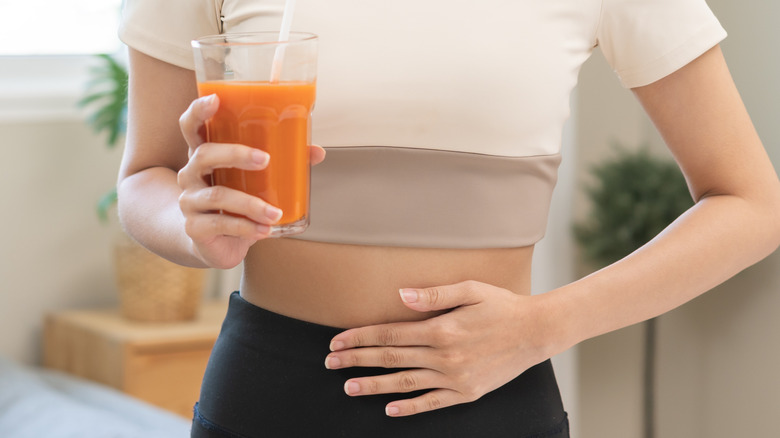 A faceless woman holding a glass of juice while touching her stomach