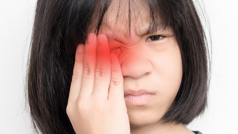 young girl covering right eye with hand