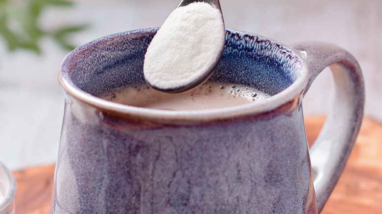 white powder spooned into blue coffee cup