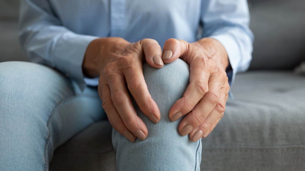 Woman holding knee, sitting on couch.