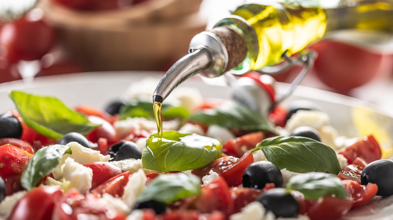 Olive oil drizzling over a caprese salad with olives