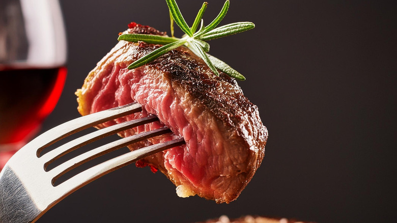 A piece of ribeye steak on a fork topped with rosemary herb