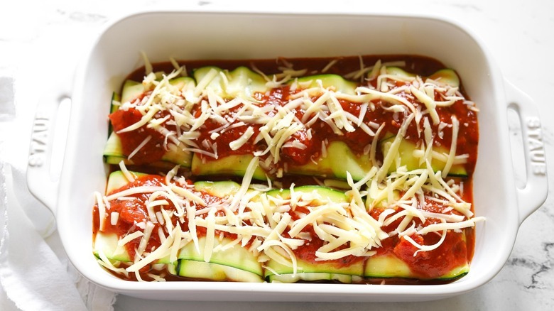 white baking dish filled with keto zucchini meat ravioli pockets topped with red pasta sauce and shredded mozzarella cheese