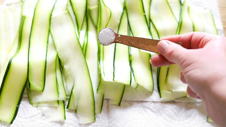 half a teaspoon of salt being sprinkled across strips of sliced zucchini