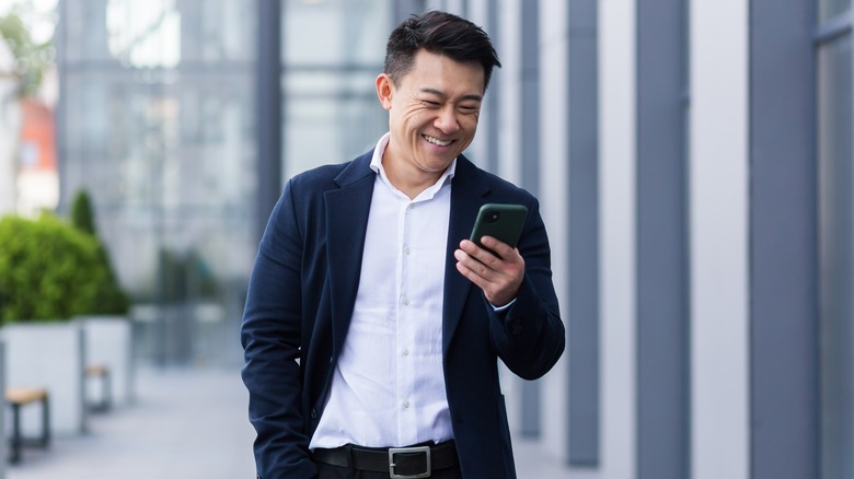 man smiling holding phone outside