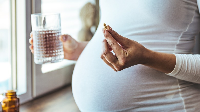 pregnant woman holding pill and glass of water