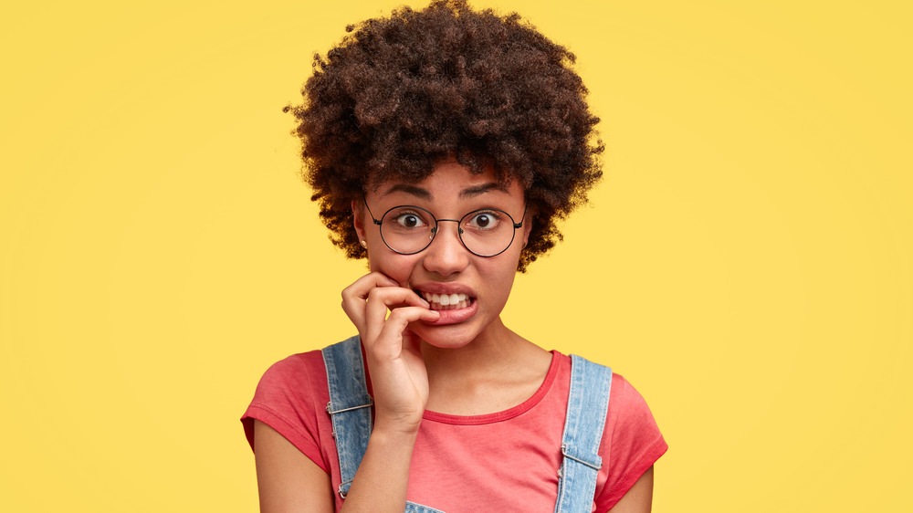 Woman against yellow background biting her nails