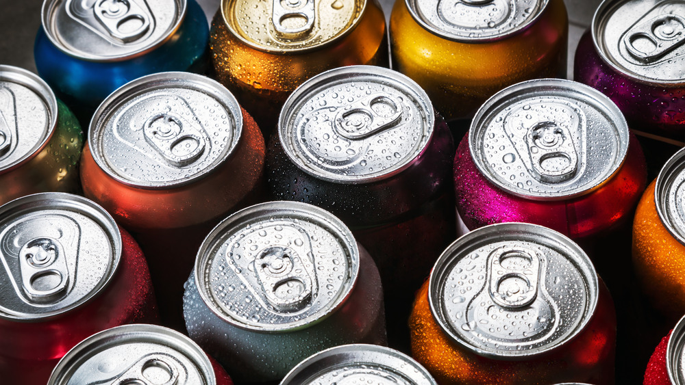 The tops of cans of soda with water droplets on most of them