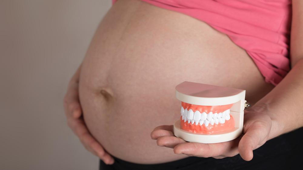 Pregnant woman holding fake teeth next to her belly