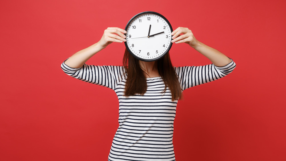 Woman in a striped shirt holding a clock in front of her face