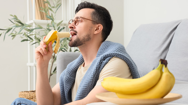 A man sitting on a couch eating a banana