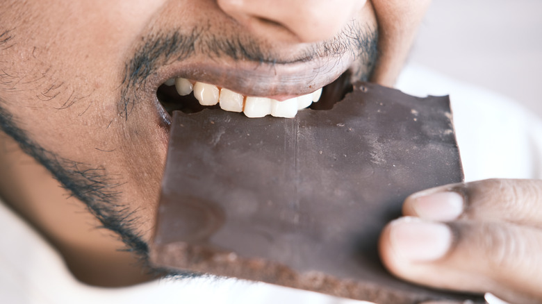 A man taking a bite of dark chocolate in close up