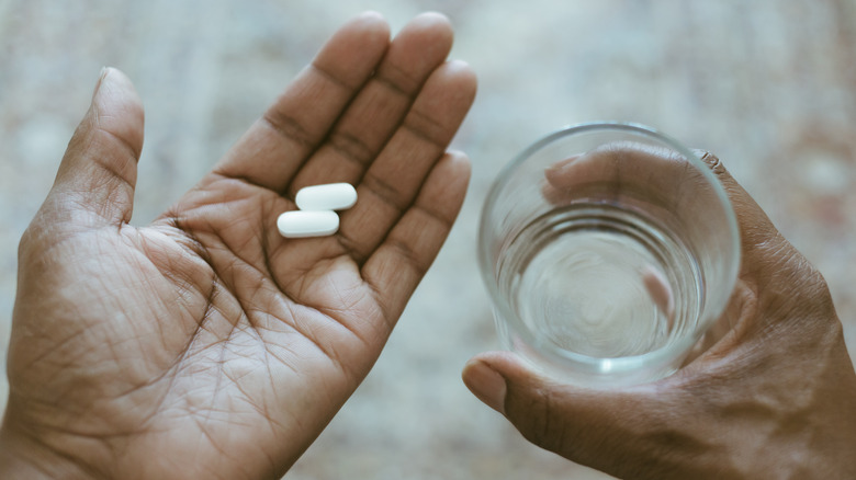 A man's hands holding two caplets and a glass of water