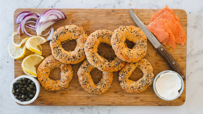 bagels, cream cheese, onions, lox and capers on cutting board