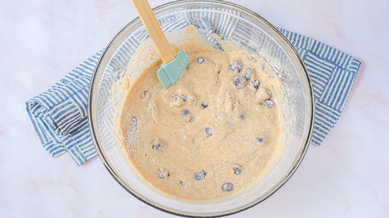 Stirring blueberries into muffin batter in a glass mixing bowl with silicone spatula