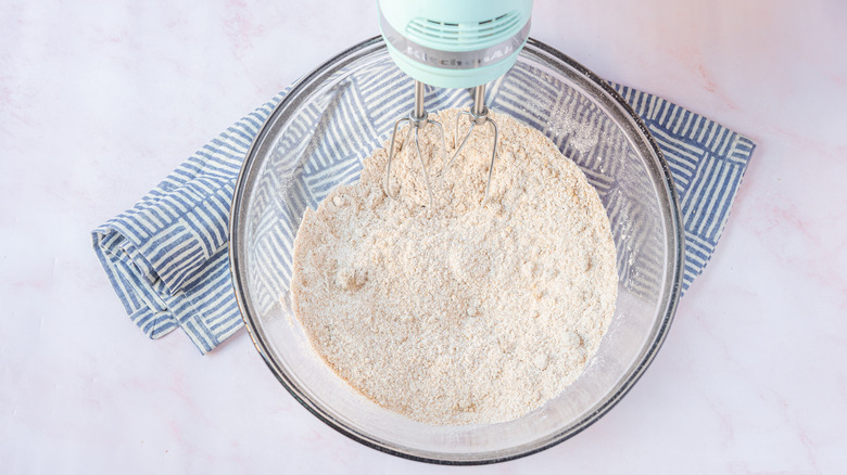 Mixing dry ingredients with a hand mixer for baking in a glass mixing bowl