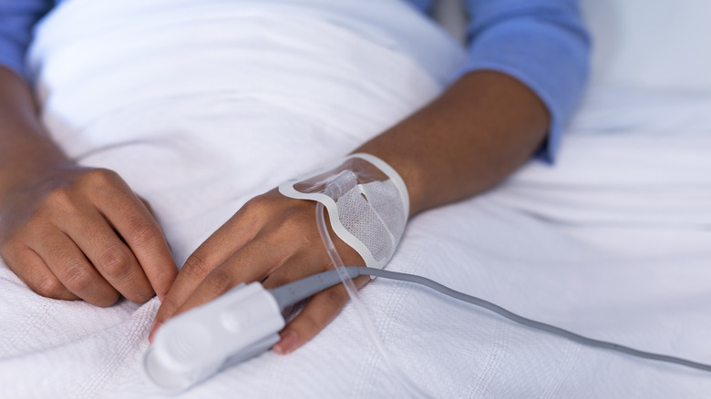 Close up of a patient's hand in their hospital bed with an IV in