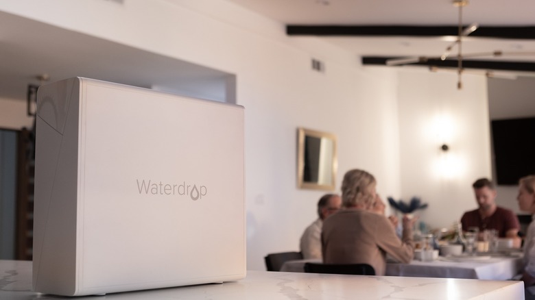 Waterdrop countertop water filter sits on counter with family in the distance at a table.