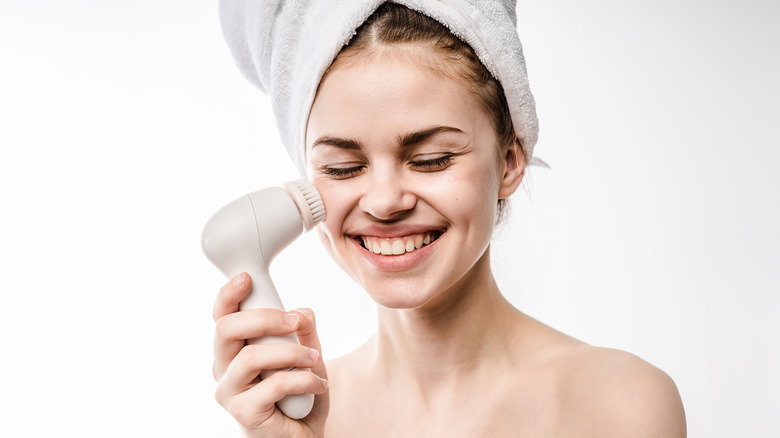 young woman using a clarisonic to clean her skin 