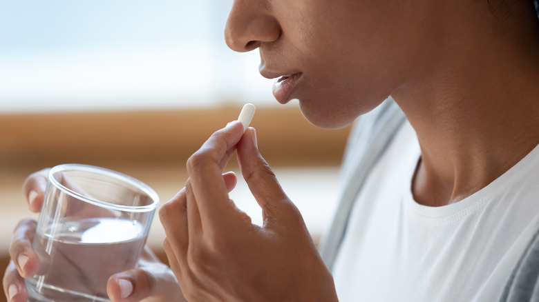 woman holding pill and water glass