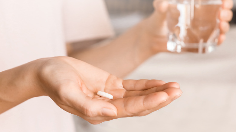 Close up of a woman's hands holding a pill and a glass of water