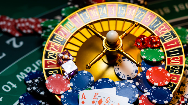 A roulette wheel covered with casino chips, dice, and cards on a roulette table
