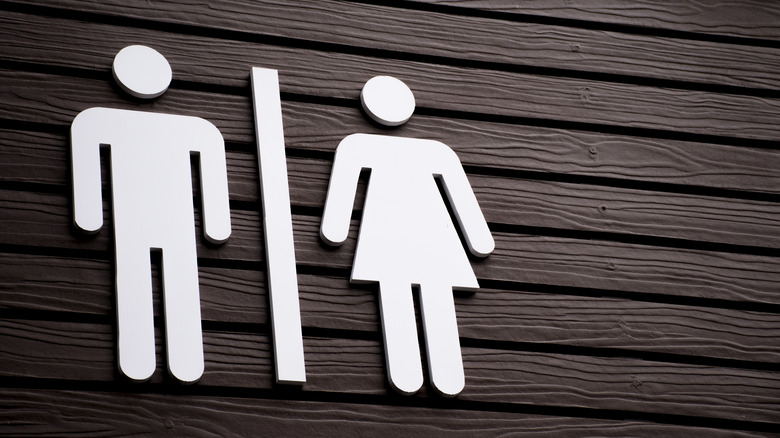 Close up of a sign for public restrooms for men and women on a painted wooden wall