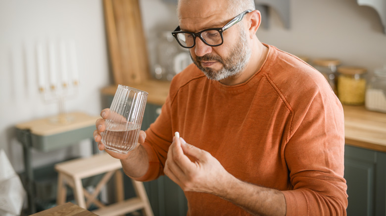 Man holding a glass of water in one hand, a pill on the other