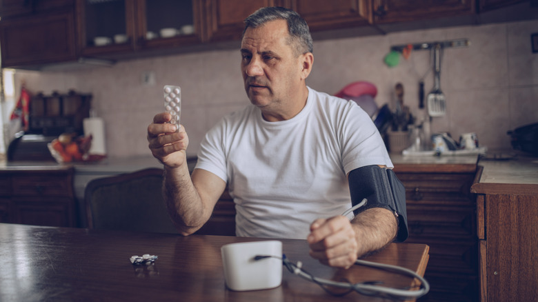 Man holding bottle of medication while taking his blood pressure