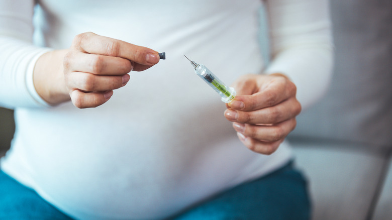 Pregnant woman uncovering syringe
