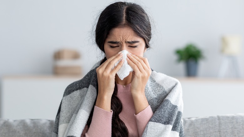 Young woman sick wrapped in a blanket and blowing her nose