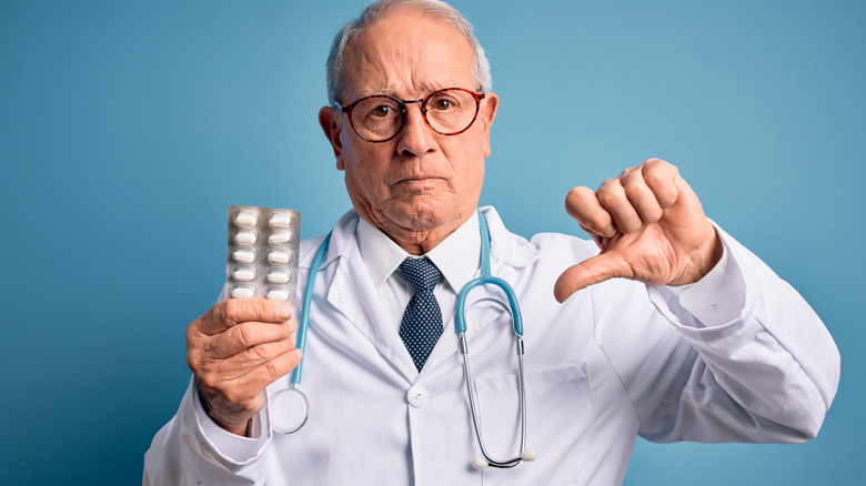 Doctor thumbs down while holding medicine